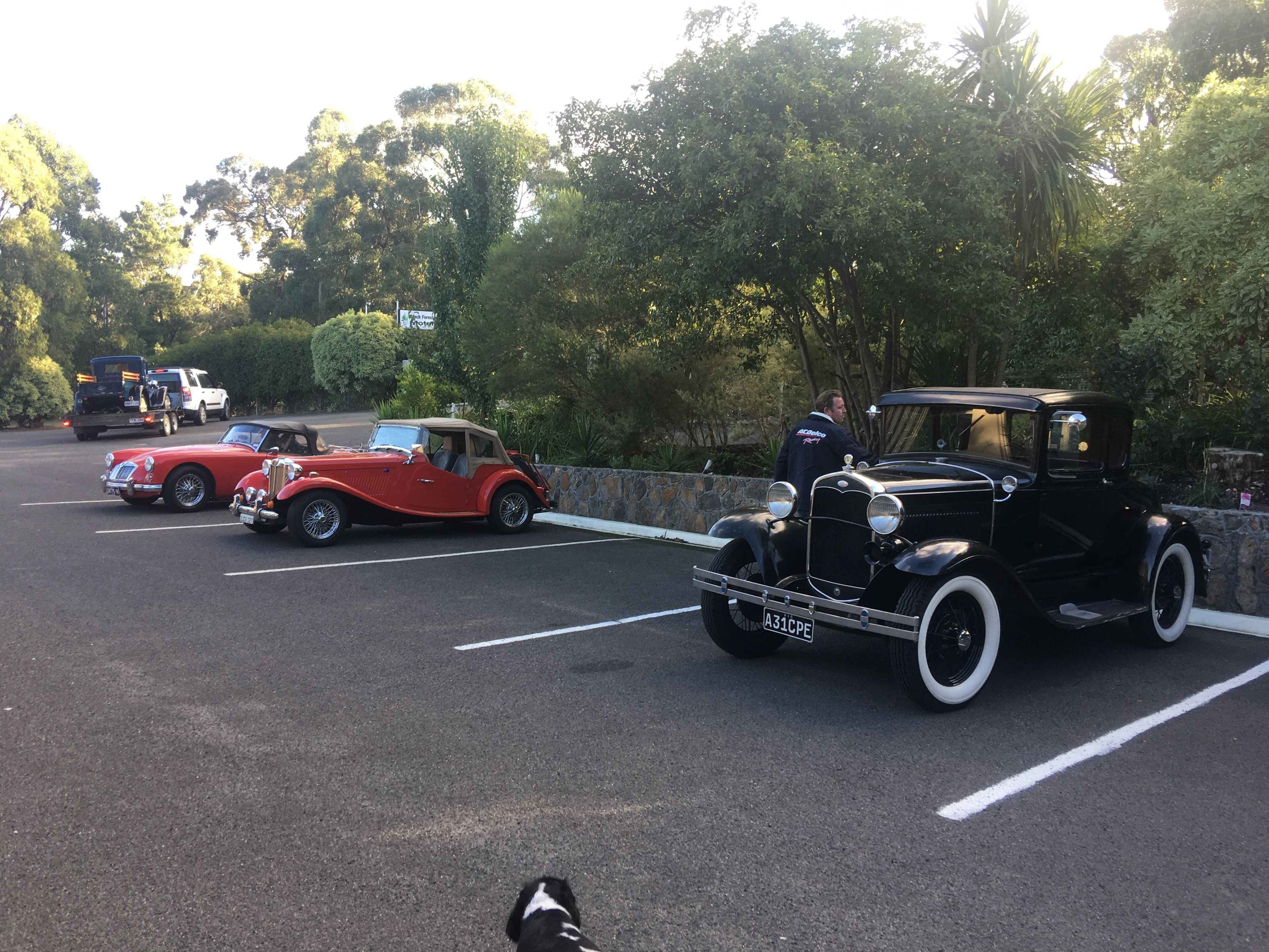Un estacionamiento con coches antiguos, incluyendo un descapotable negro y un deportivo rojo.