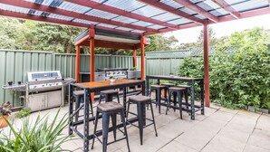 Un patio exterior con una parrilla, taburetes de bar y una mesa.