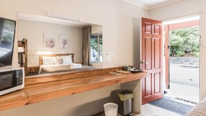 Habitación de hotel con un escritorio de madera, una cama con ropa blanca, un televisor y vistas al exterior a través de una puerta.
