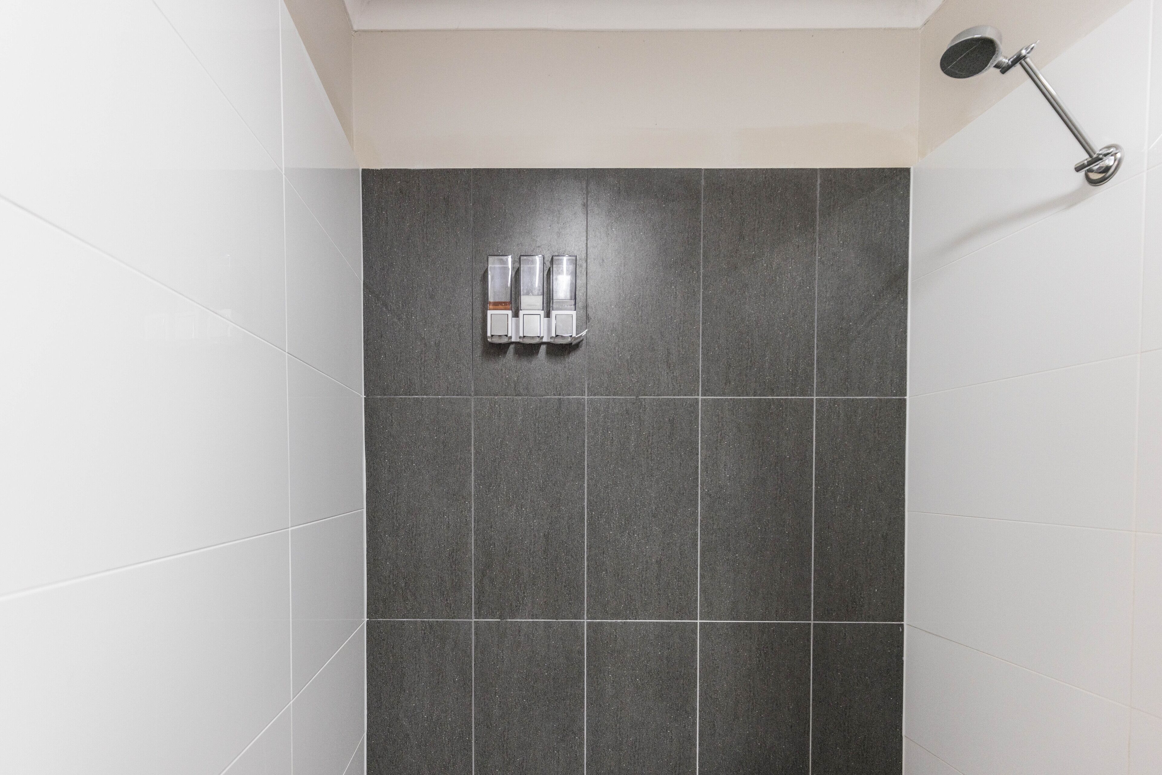 A bathroom with dark grey tiles, a showerhead, and two soap dispensers.