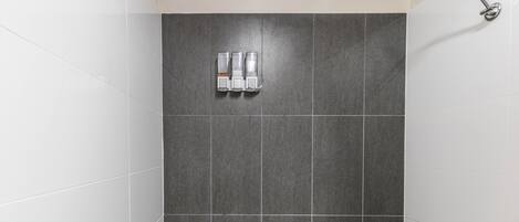 Um banheiro com azulejos cinza escuro, um chuveiro e dois dosadores de sabonete.