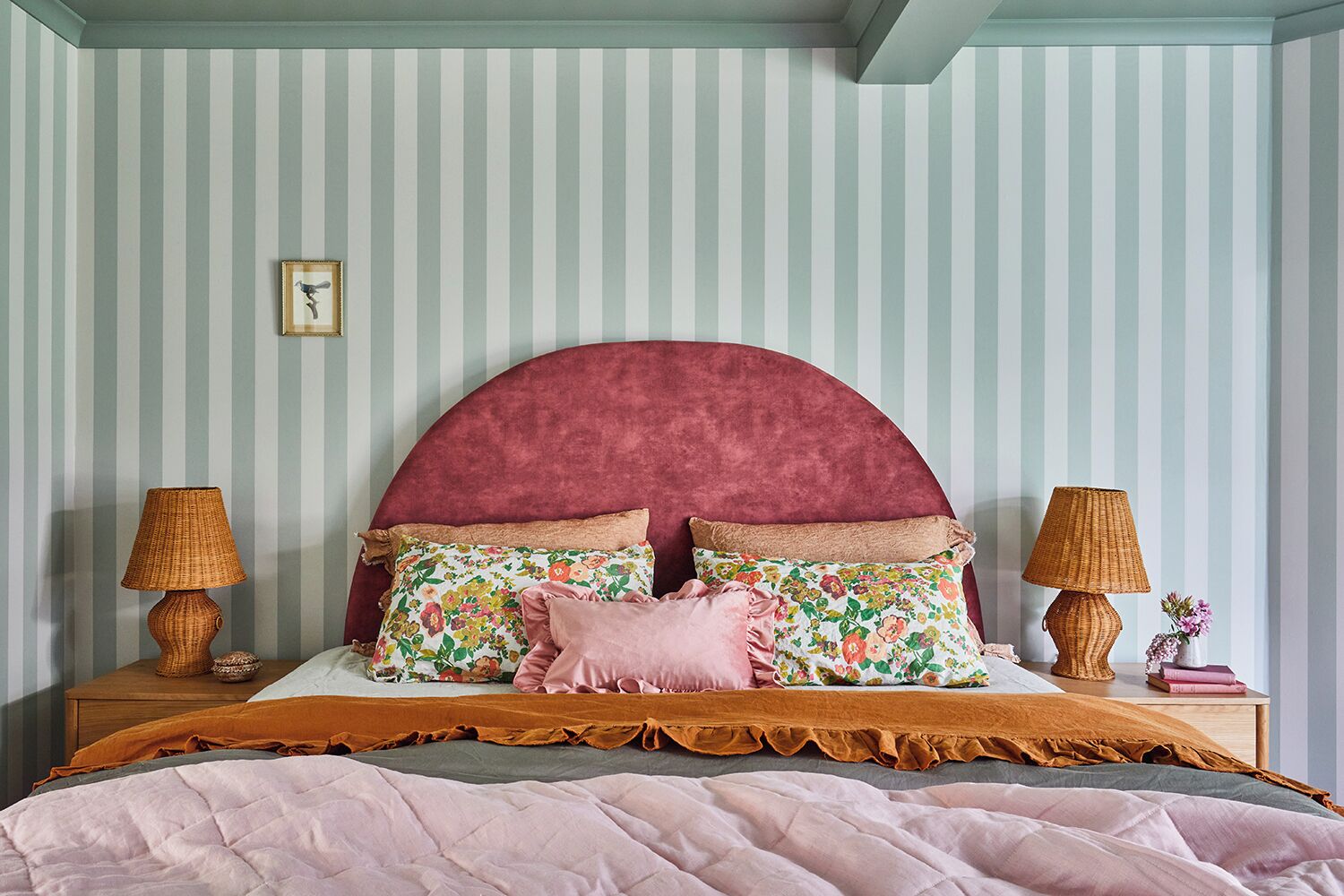 Una cama con cabecera curvada, dos lámparas de noche y un cojín estampado con motivos florales.