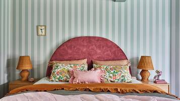 Una cama con cabecera curvada, dos lámparas de noche y un cojín estampado con motivos florales.
