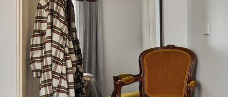 A room with a bed, a chair, a coat rack with hats, and a mirror.