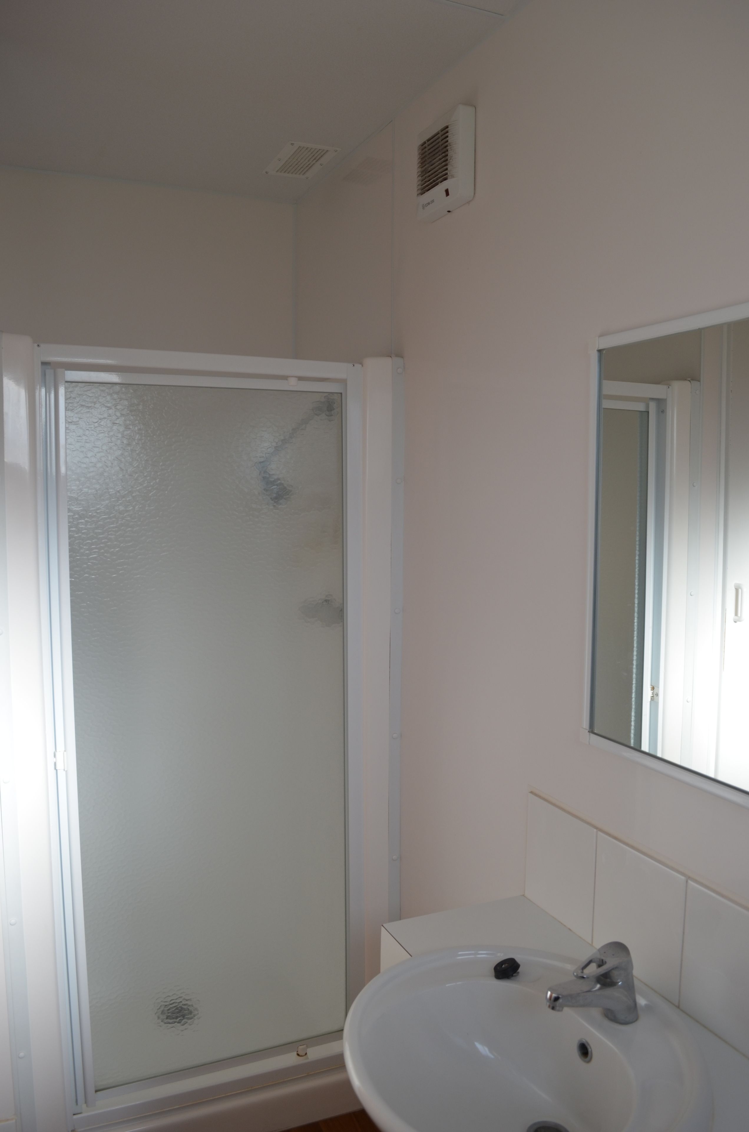 Ein Badezimmer mit Duschkabine aus Glas, einem Waschbecken und einem Spiegel.