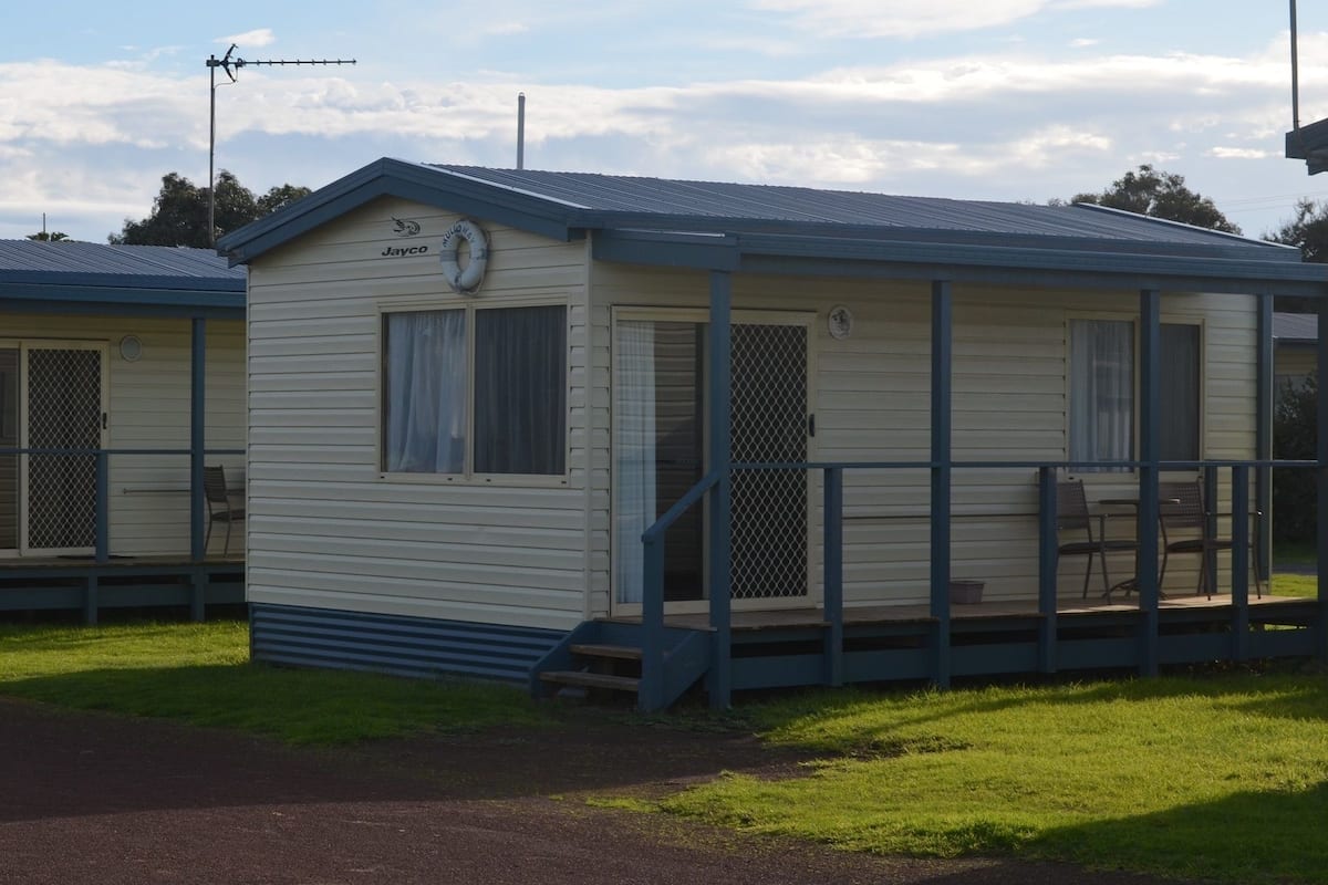 A small, single-story mobile home with a porch and a small deck.