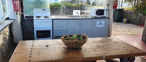A rustic outdoor kitchen with a stove, microwave, and a sign indicating it's a sandwich maker.