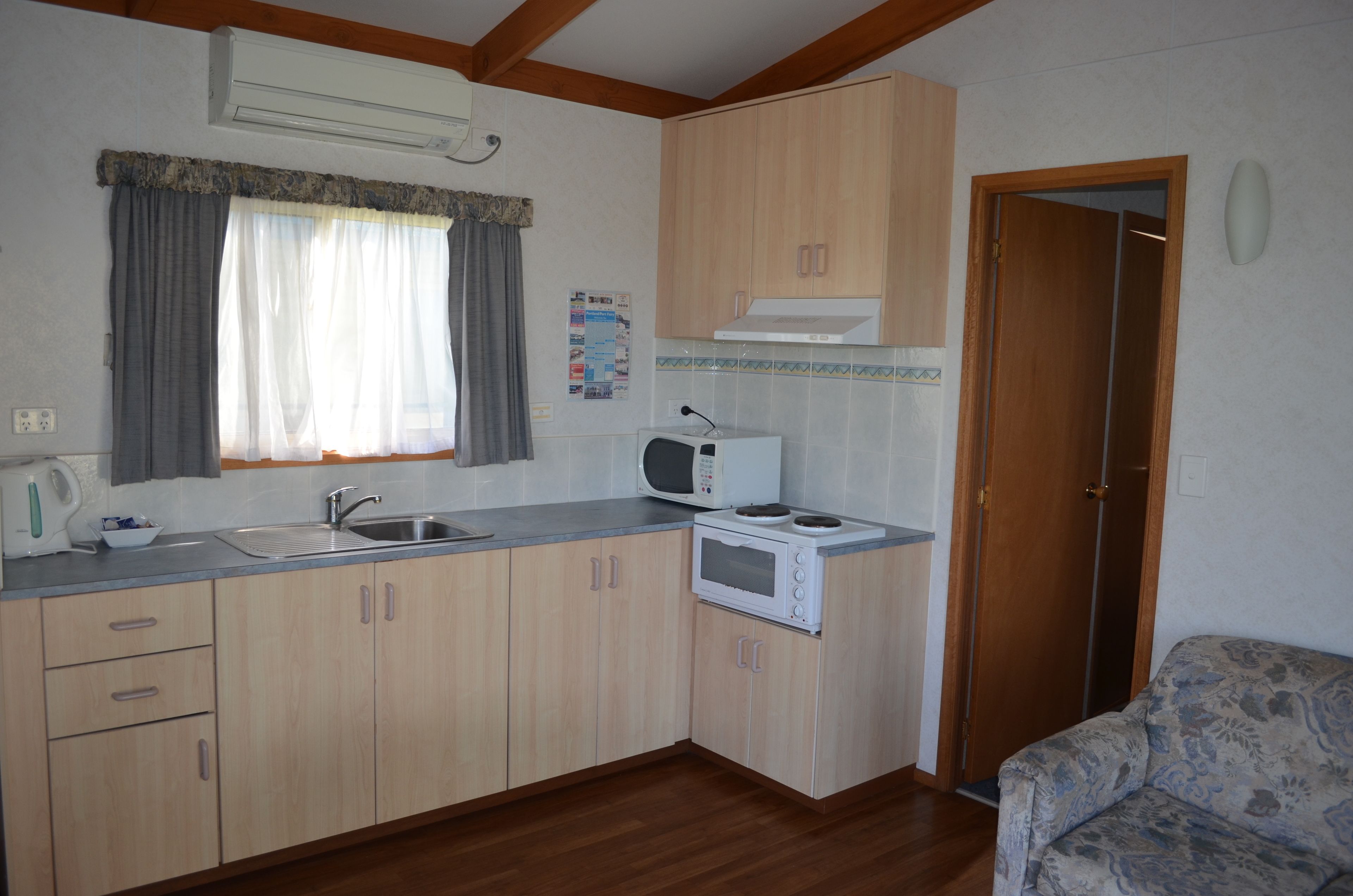 Una cocina compacta con armarios de madera, un microondas, una tetera y un lavamanos.