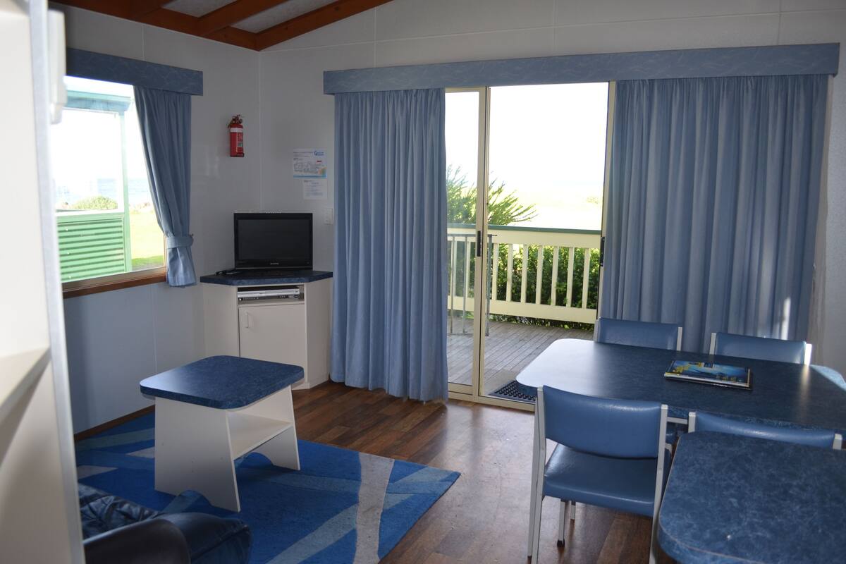 A room with a kitchenette, a dining table with chairs, a television, and a sliding glass door leading to an outdoor area.