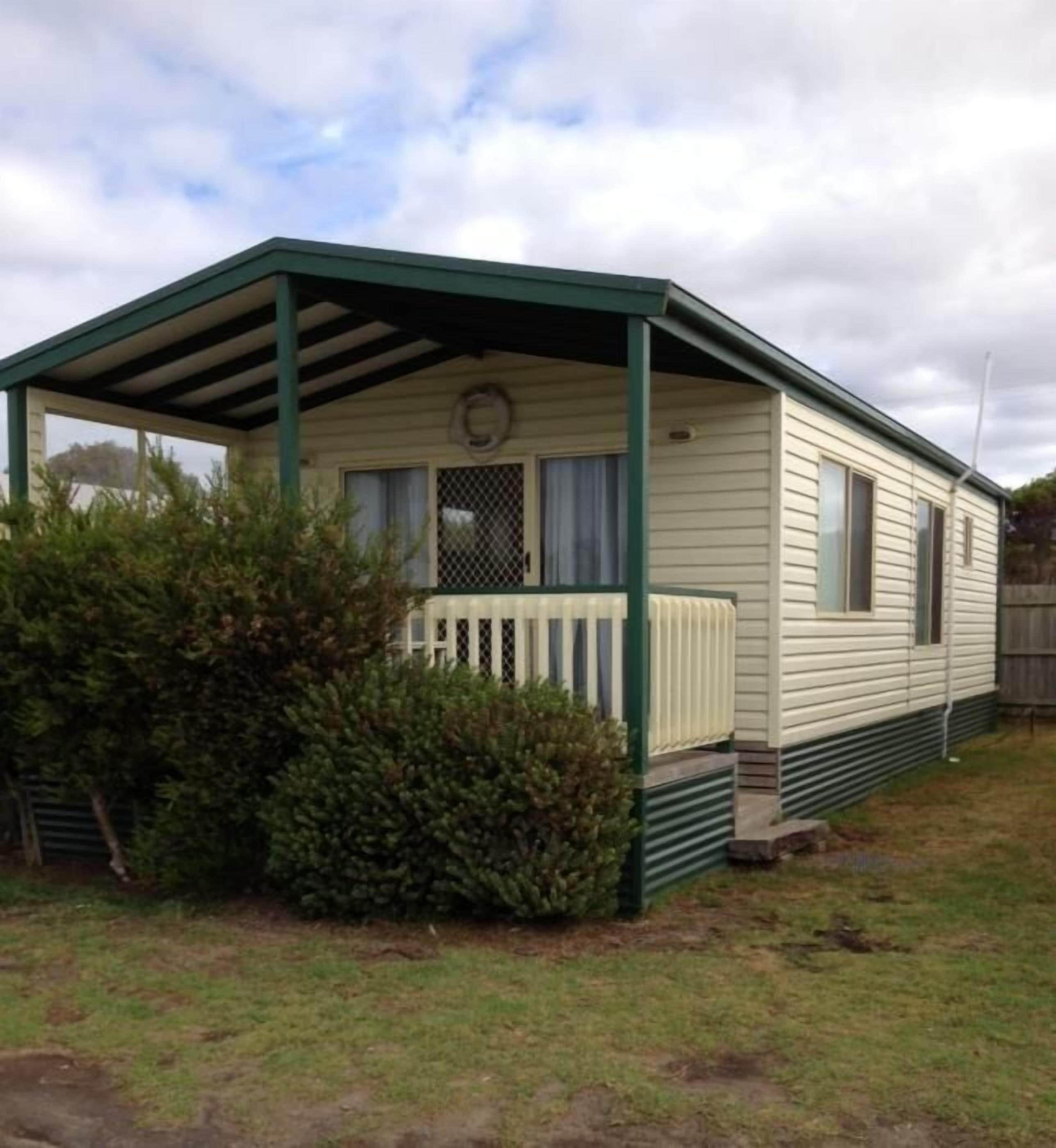 A mobile home with a covered porch, a fenced yard, and a small garden area.