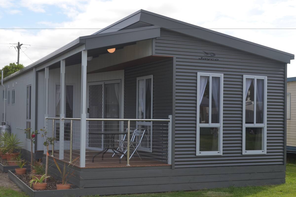A single-story mobile home with a covered porch, a small outdoor seating area, and a fenced garden.