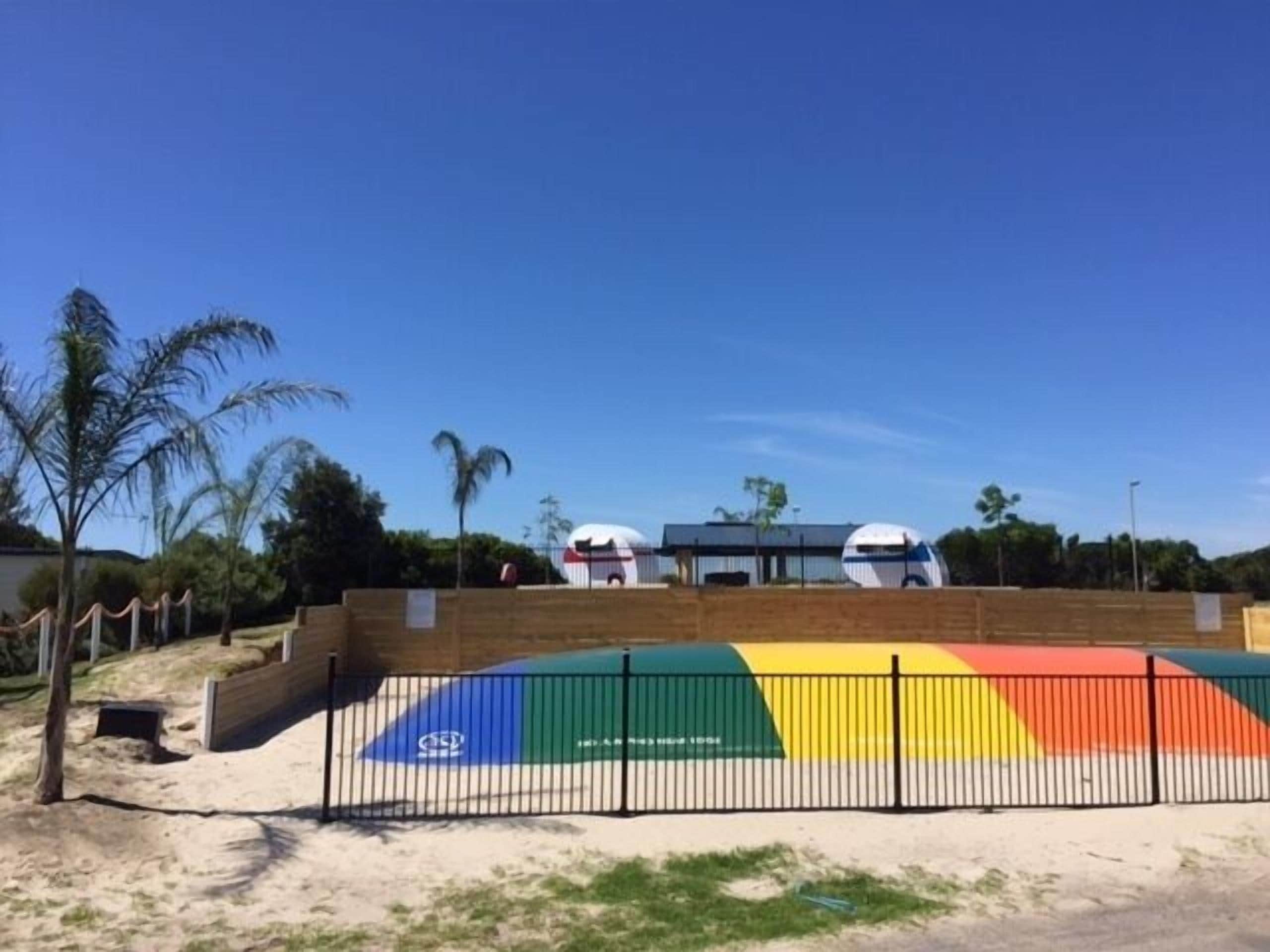 A fenced area with a colorful mural, a palm tree, and a building with two domed structures in the background.
