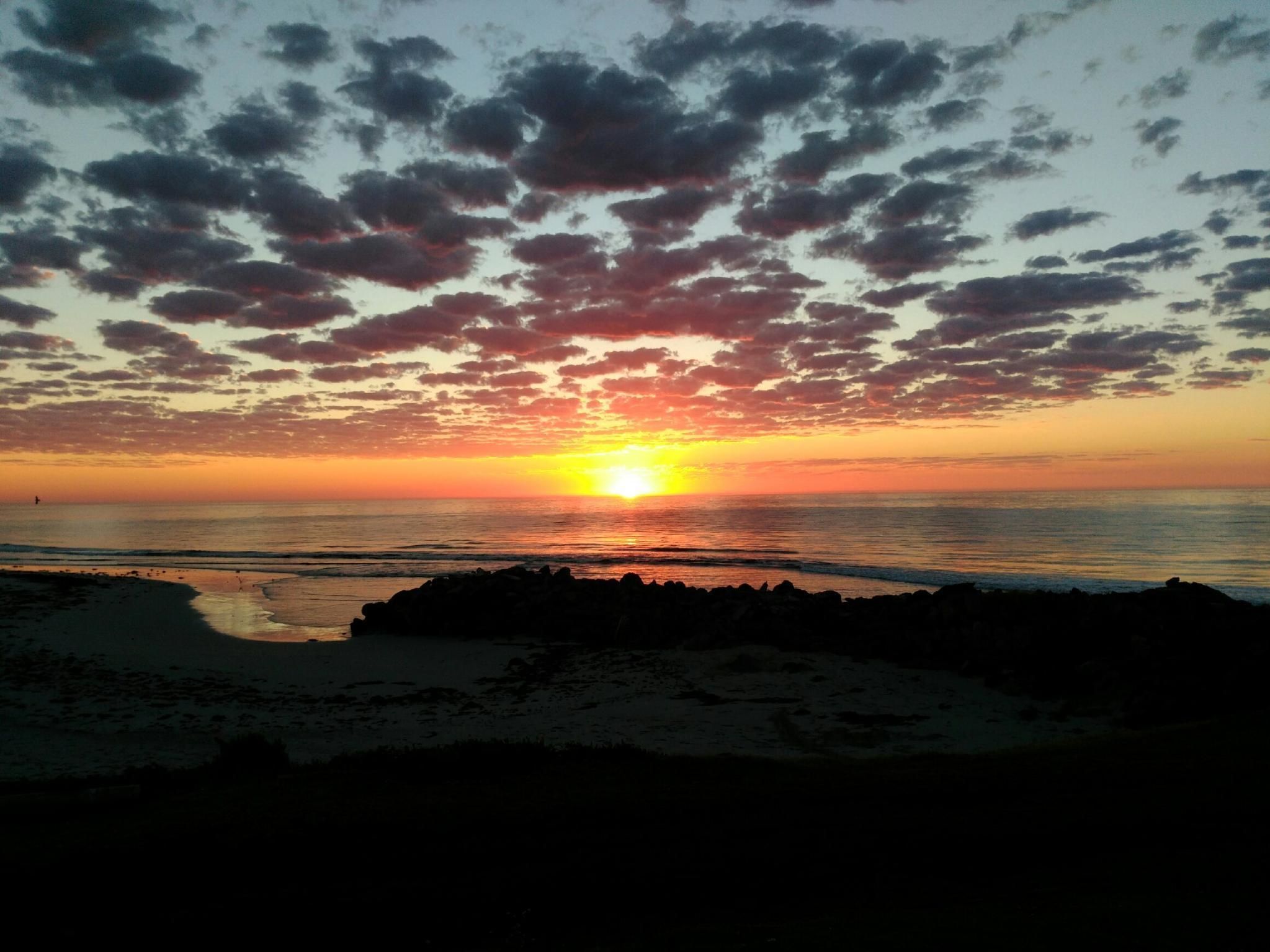 Un atardecer sobre una playa con costa rocosa.
