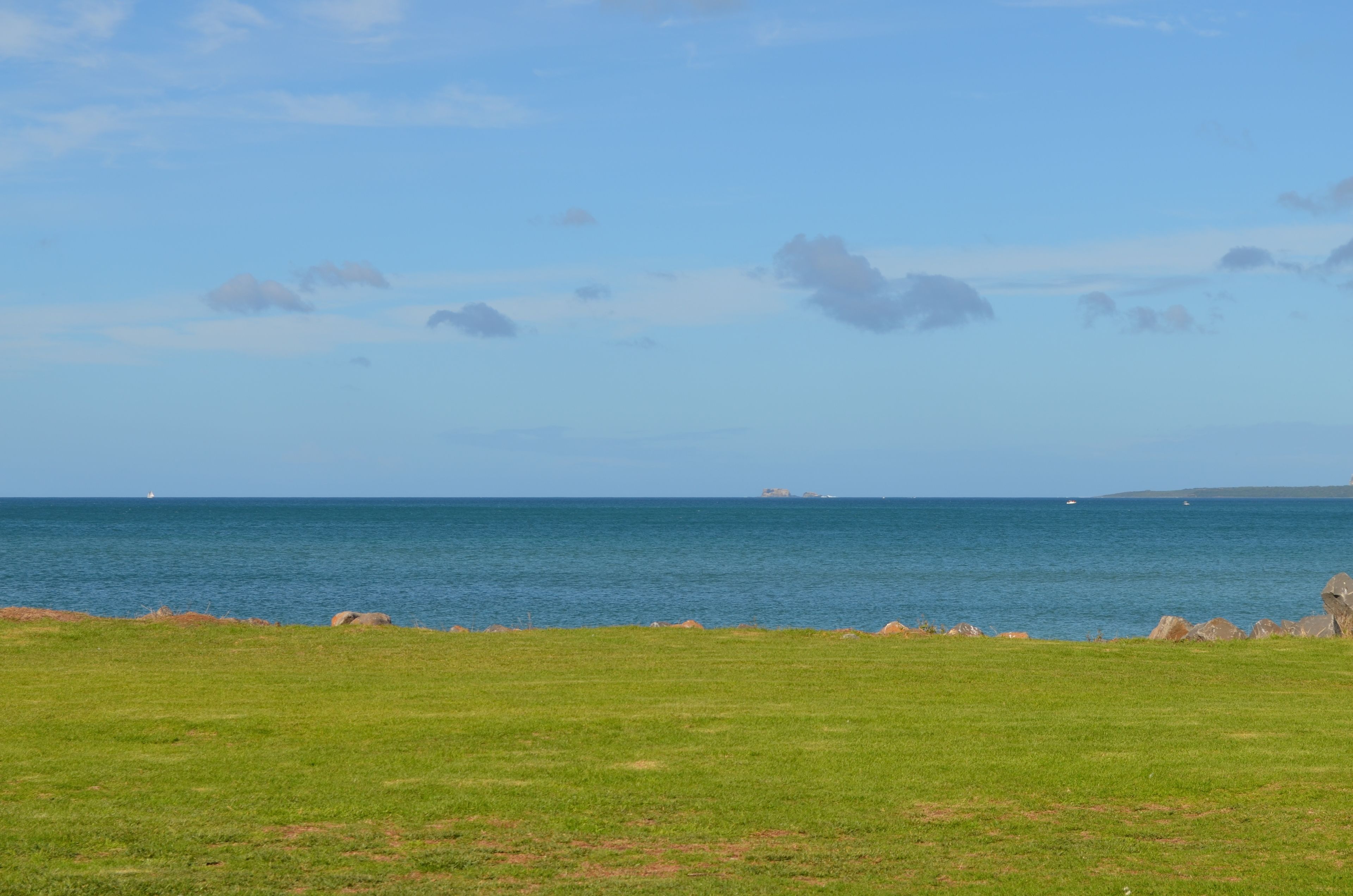 A grassy field with a view of the sea and distant land.