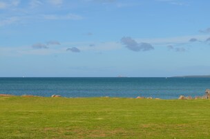A grassy field with a view of the sea and distant land.