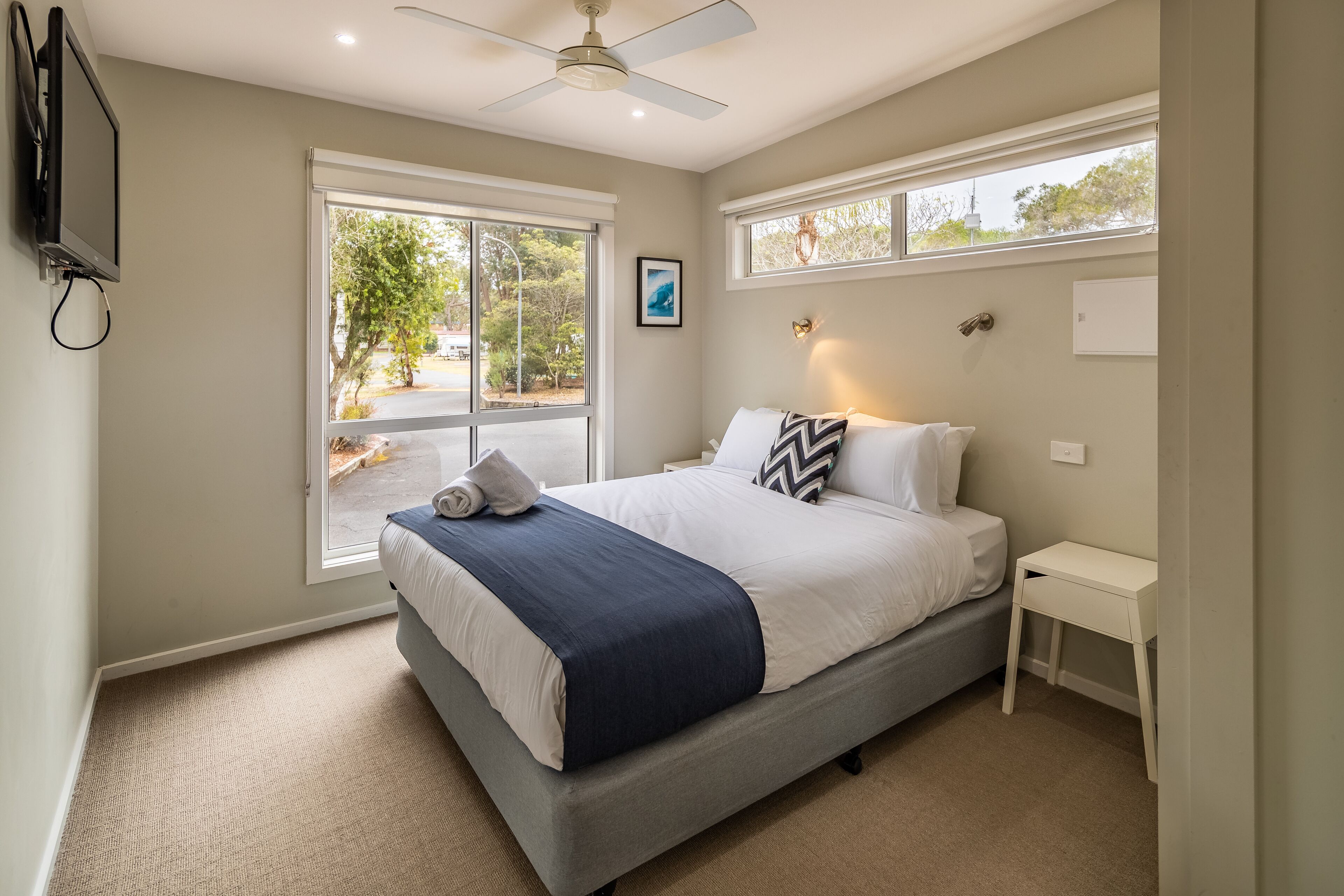 Une chambre à coucher comprenant un lit, une table de chevet, un ventilateur de plafond et une fenêtre donnant sur l’extérieur.