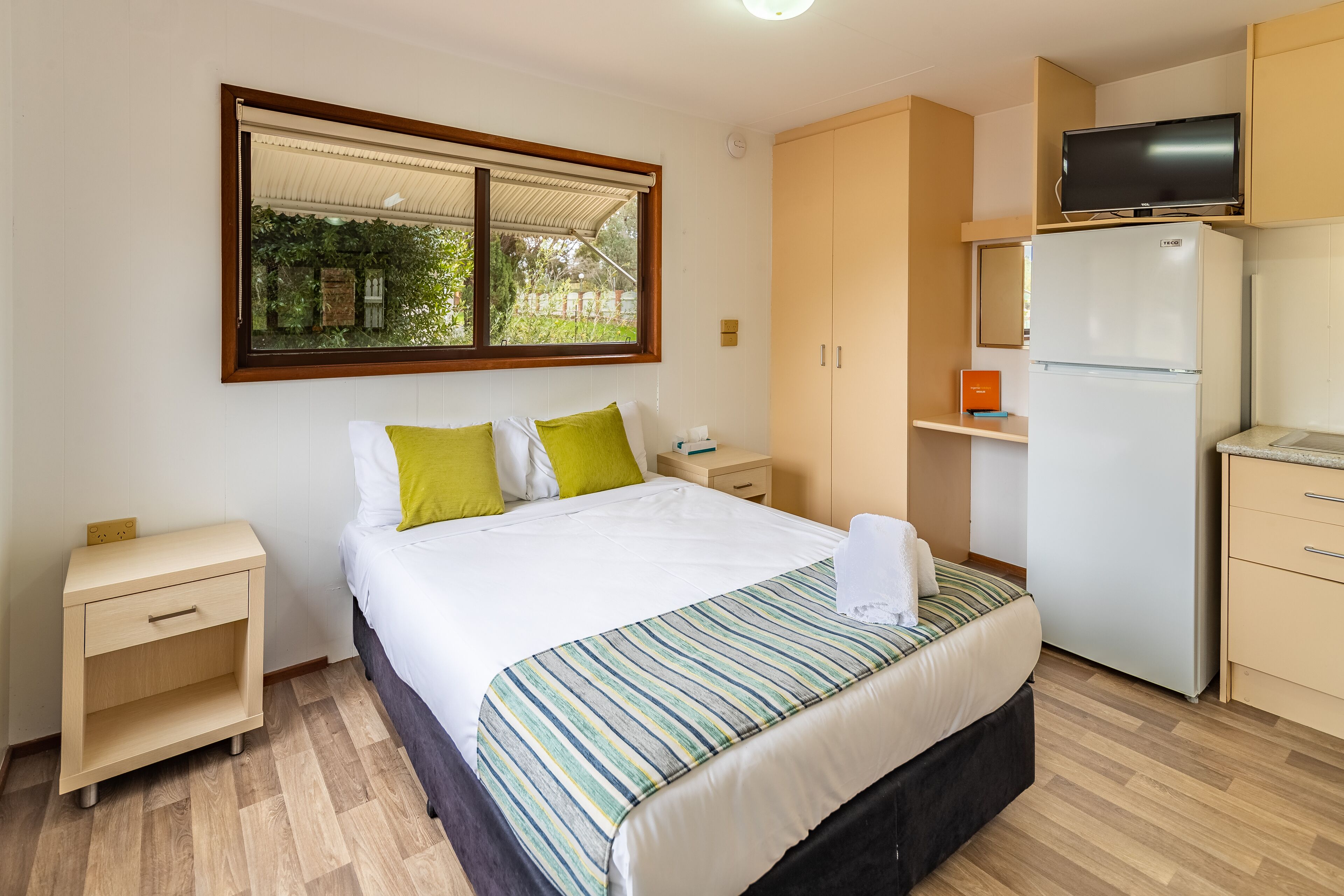 Een hotelkamer met een bed, nachtkastje, kledingkast, koelkast en televisie.