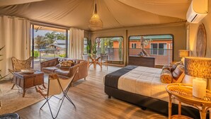 A spacious tented room with a large bed, a dining area, and a view of the outside. - NRMA Broulee Holiday Park (Broulee)