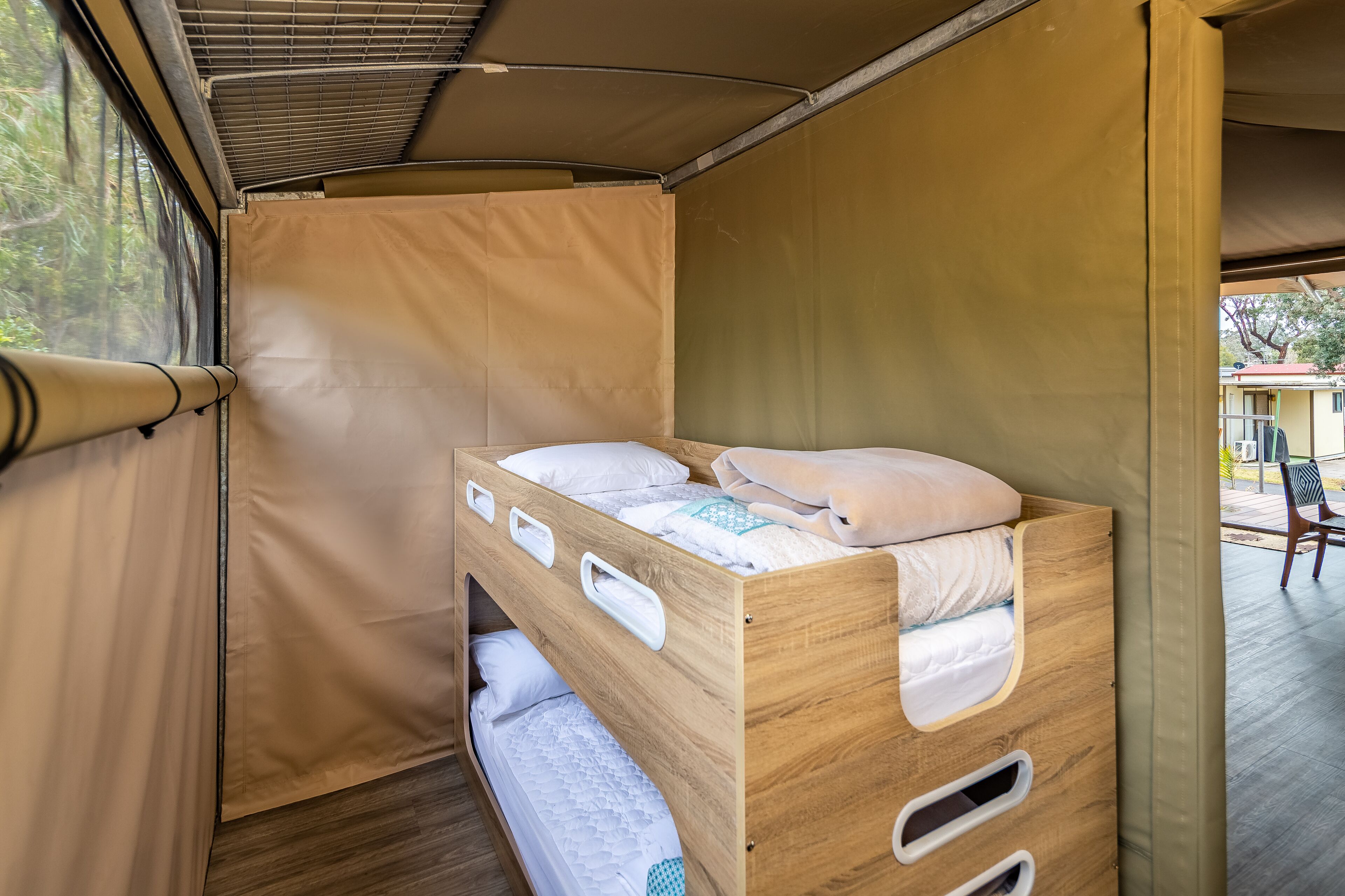 Habitación pequeña con una cama individual, una litera de madera, una ventana que da a zonas verdes y una cortina.