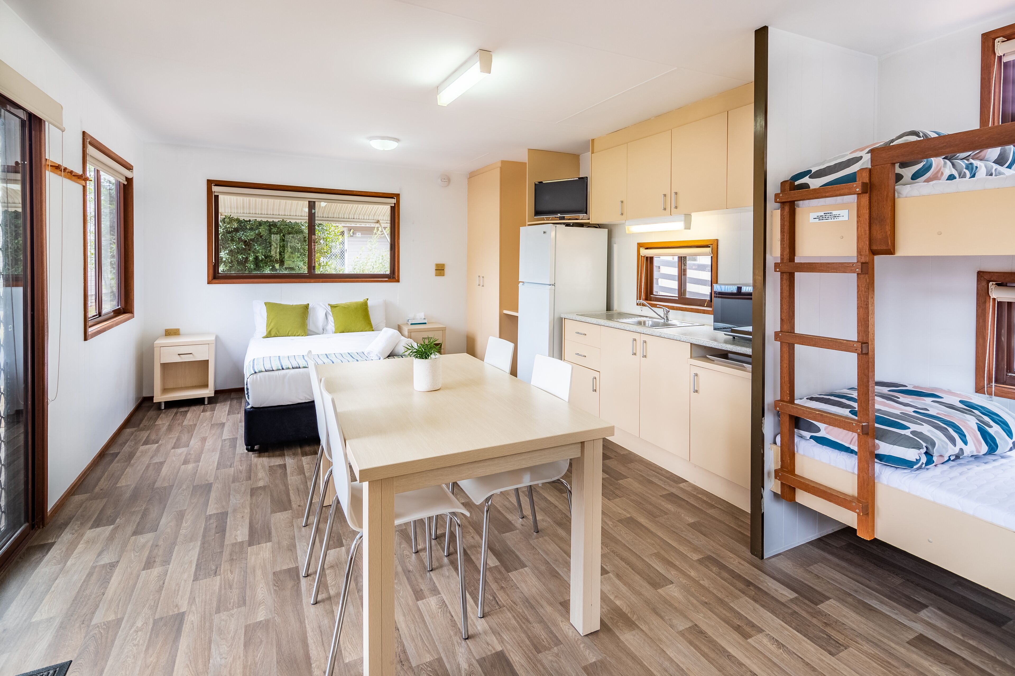 A compact room with a bunk bed, a small kitchenette, a dining area, and a window with a view of greenery.