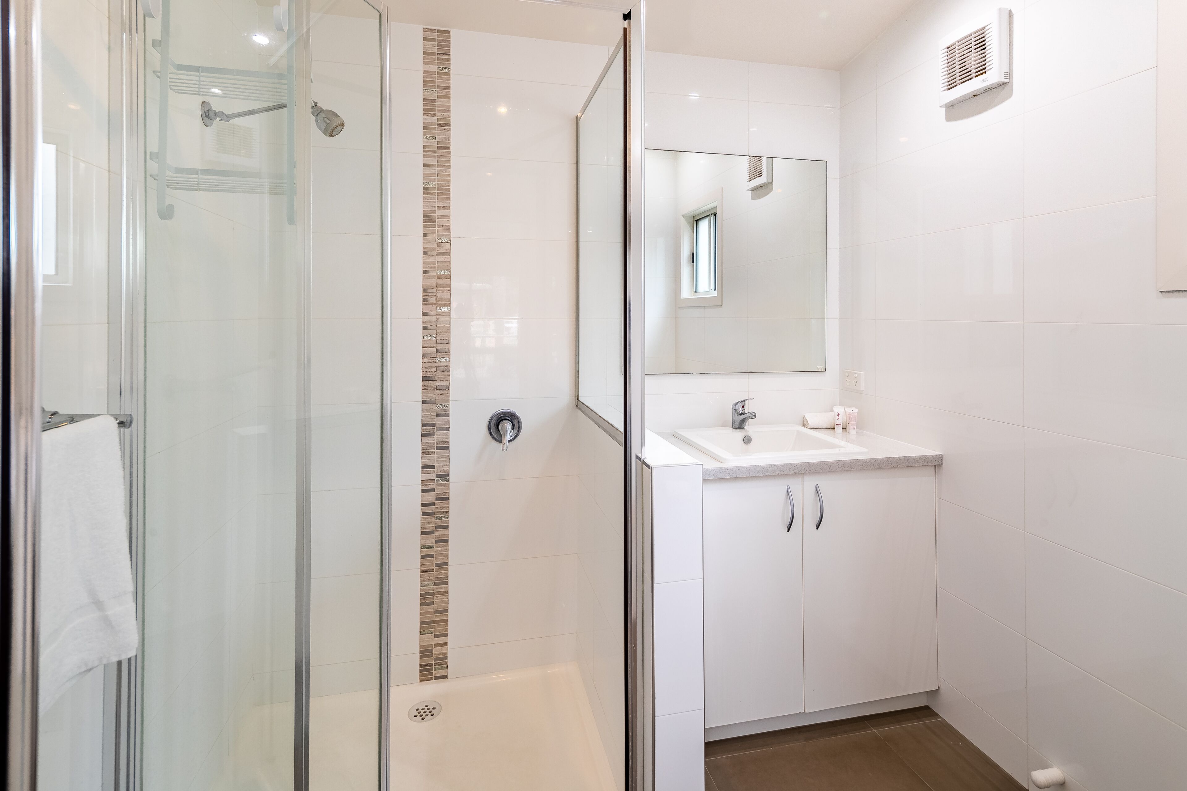 A modern bathroom with a glass-enclosed shower, a white sink with a mirror, and a tiled wall.