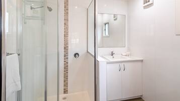 A modern bathroom with a glass-enclosed shower, a white sink with a mirror, and a tiled wall.