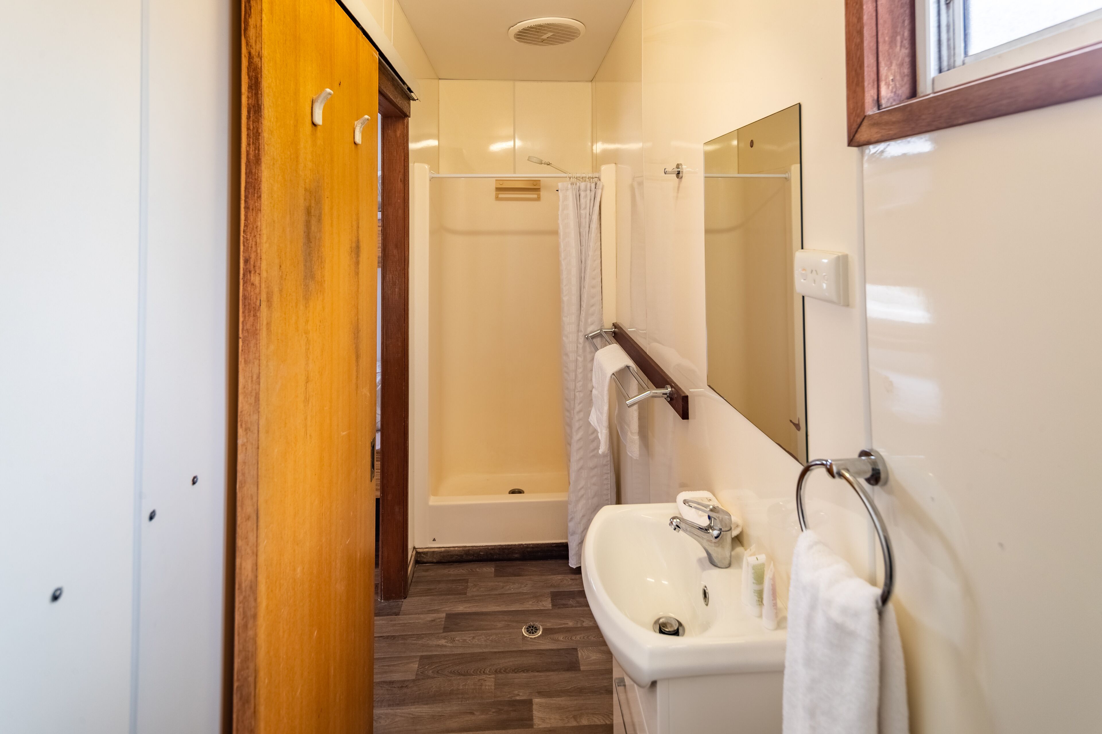 Een badkamer met een houten garderobe, een witte wastafel, een spiegel en een douche.