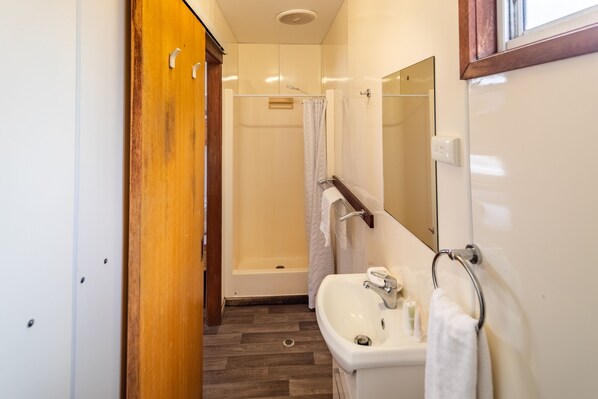 A bathroom with a wooden wardrobe, a white sink, a mirror, and a shower area. - NRMA Broulee Holiday Park (Broulee)