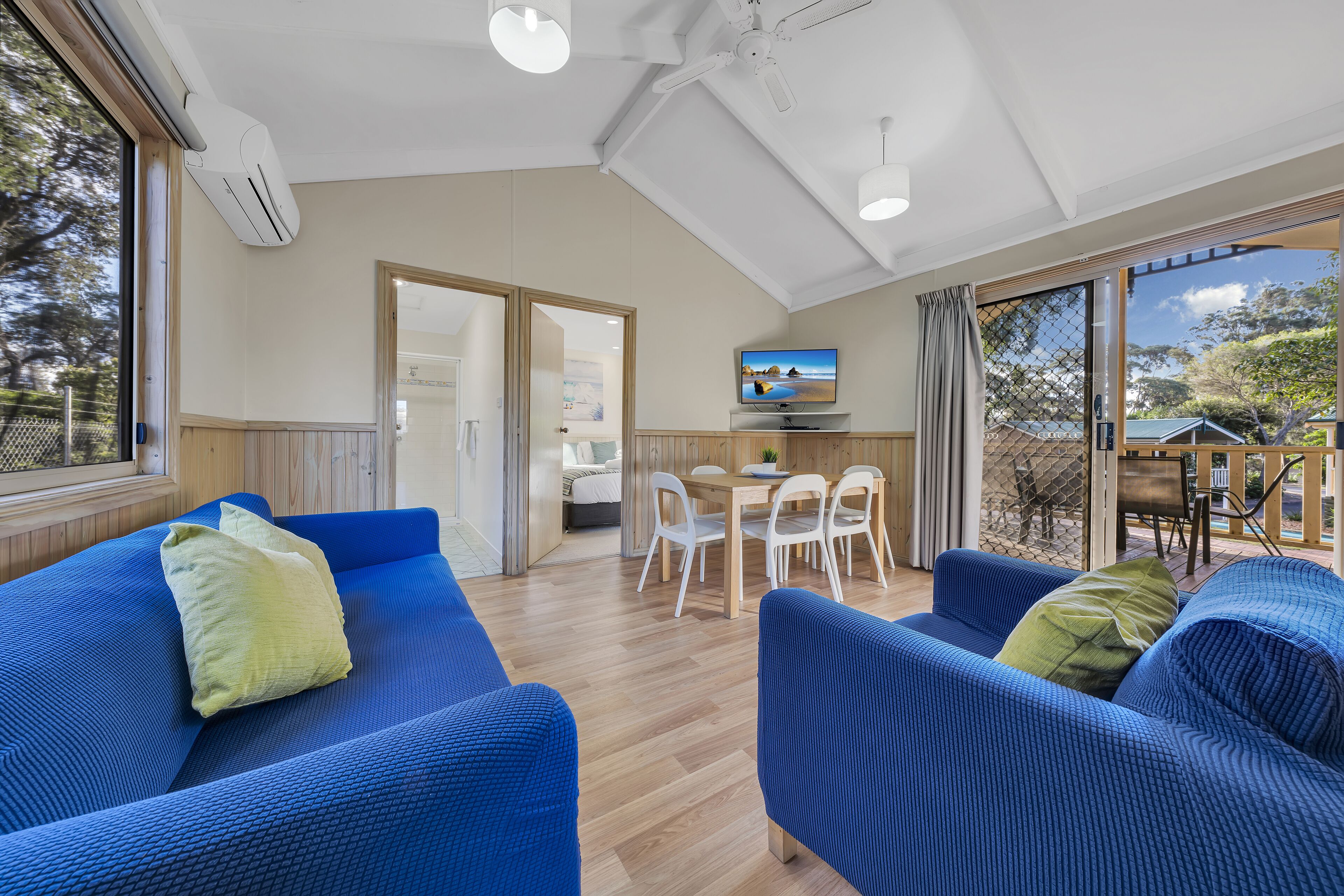 A modern living room with blue sofas, a wooden dining table, and a TV.