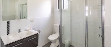Ein modernes Badezimmer mit einer Glaskabine zur Dusche, einem weißen Waschbecken und einem dunklen Schminktisch.