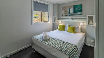 A neatly arranged hotel room with a bed, a window, a painting, and a shelf with decorative items.