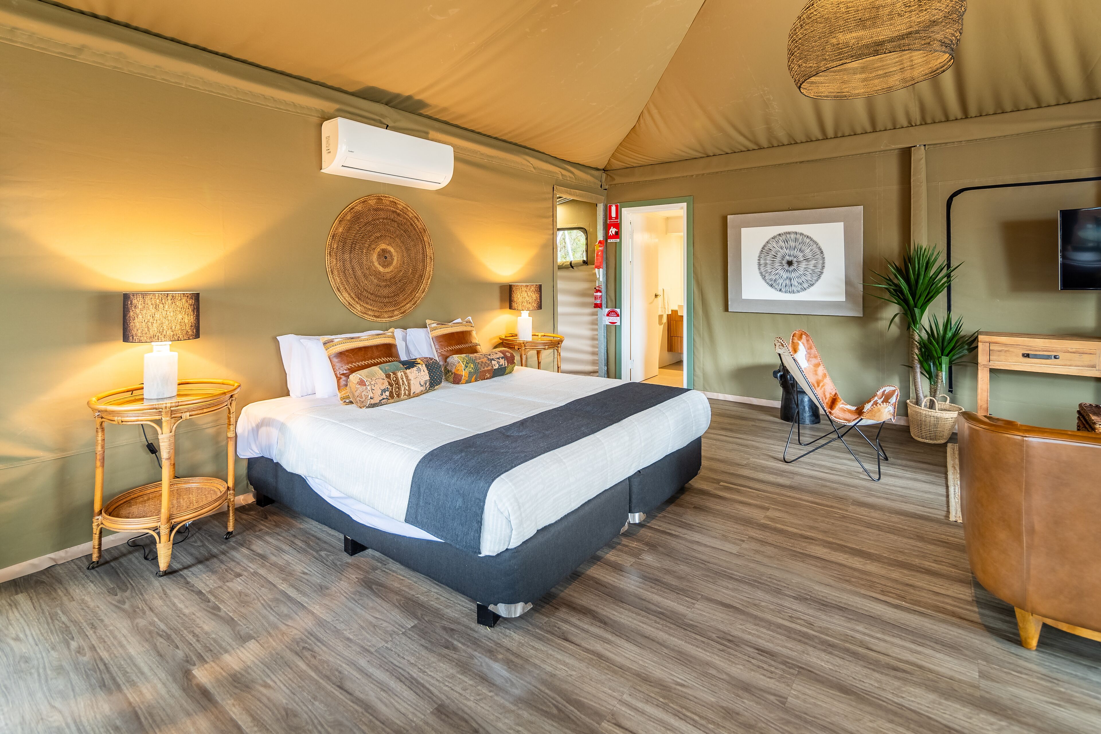 A spacious bedroom with a large bed, bedside tables, a television, and a door leading to another room.