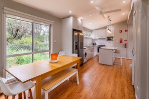 Una cocina moderna con una mesa de comedor de madera, sillas blancas y vistas a zonas verdes.