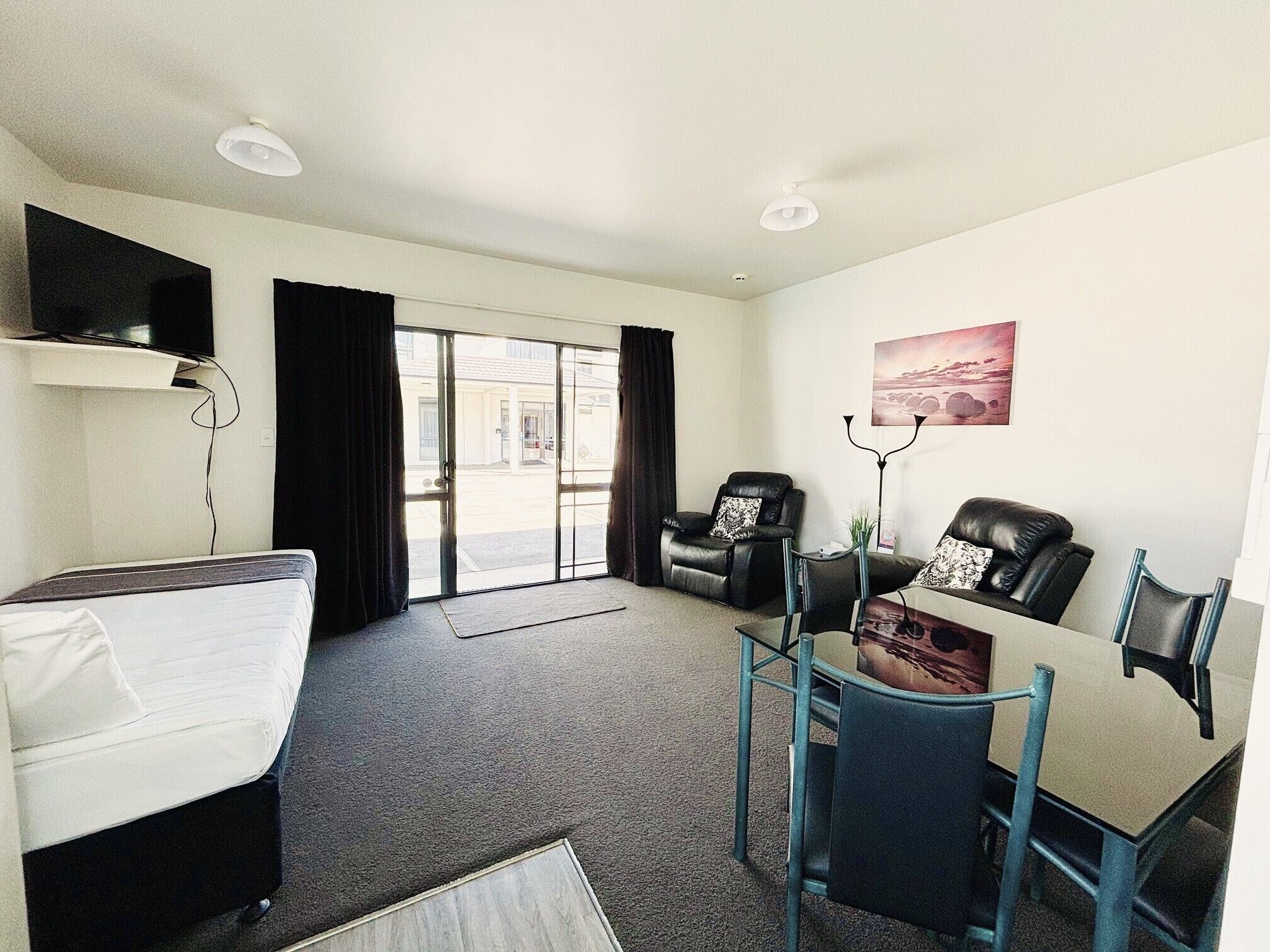 A hotel room with a bed, a desk, two chairs, a sofa, and a large window with curtains.