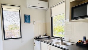 Una cocina compacta con aire acondicionado integrado, un refrigerador pequeño, un lavamanos y un microondas.
