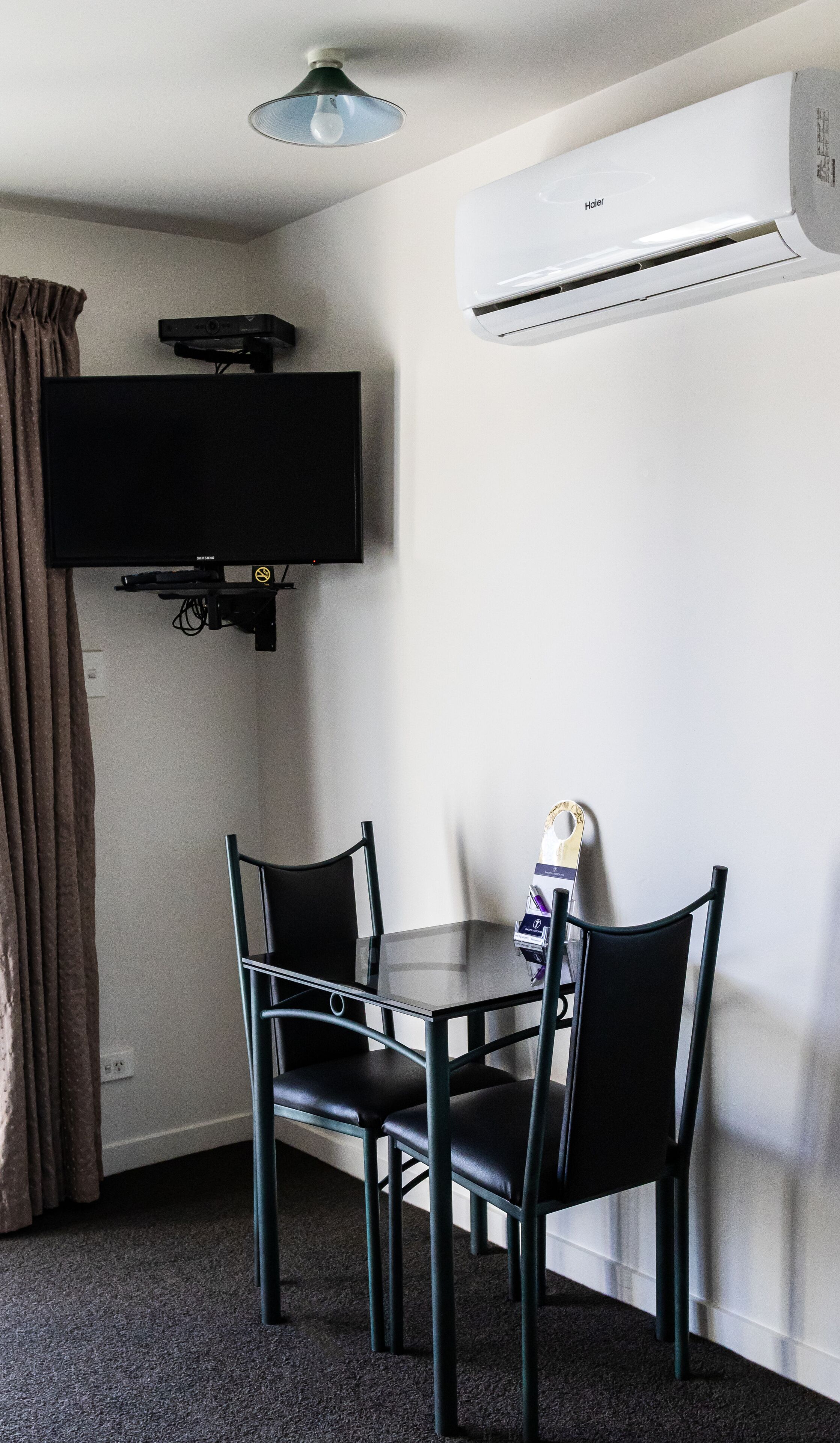 Una habitación pequeña con un televisor montado en la pared, una mesa con dos sillas y un equipo de aire acondicionado.