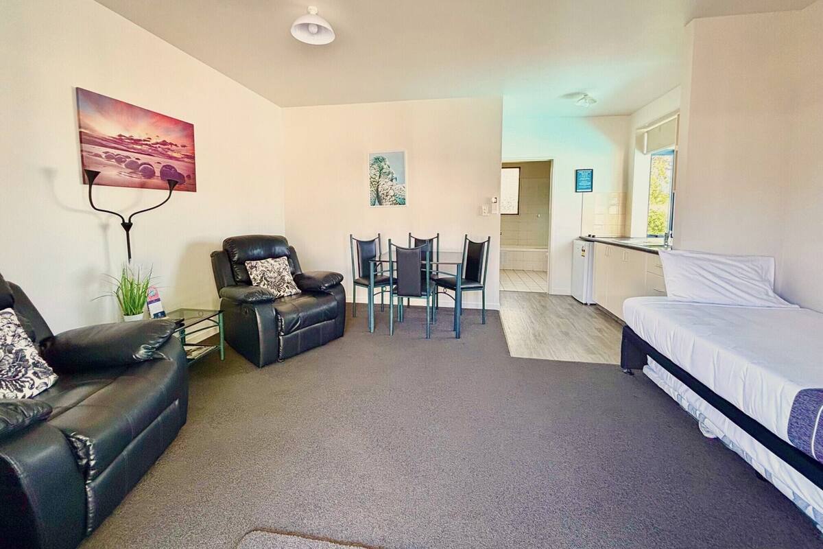 A compact living space with a sofa, a dining table with chairs, a kitchenette, and a bed.