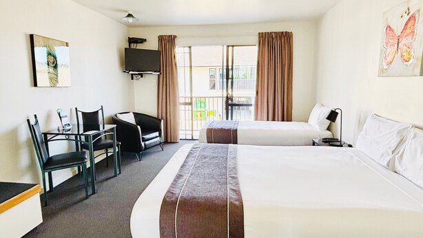 Habitación de hotel con dos camas, un escritorio con silla, televisor montado en la pared y balcón con cortinas.