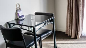Una habitación pequeña con una mesa, una silla, un televisor montado y una cortina.