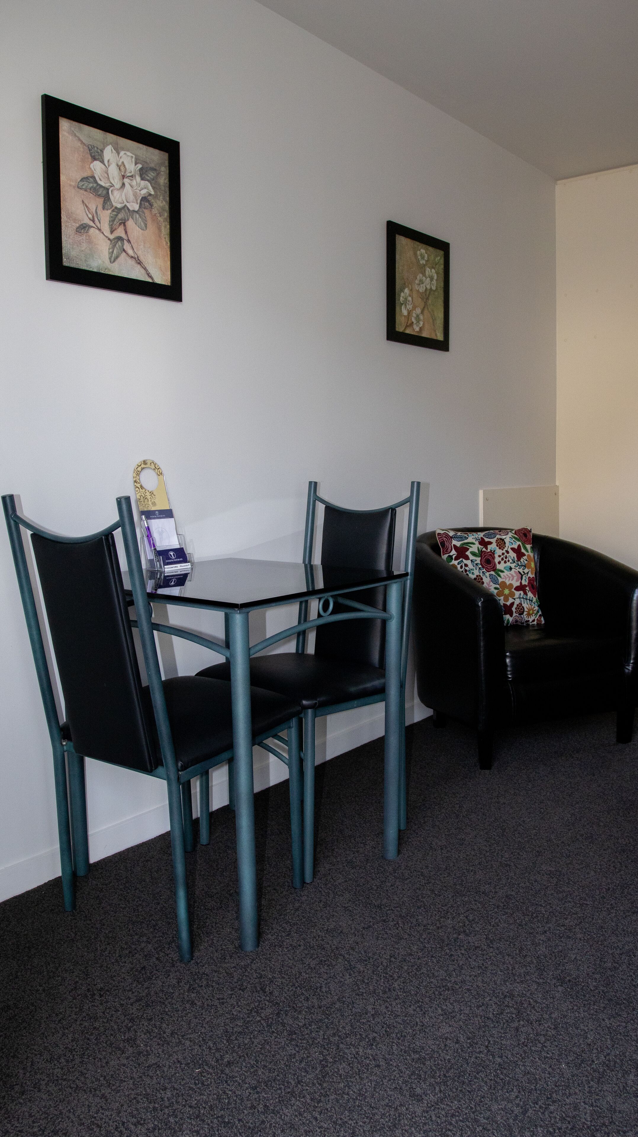 A room with a table and two chairs, a couch, and two framed floral paintings on the wall.