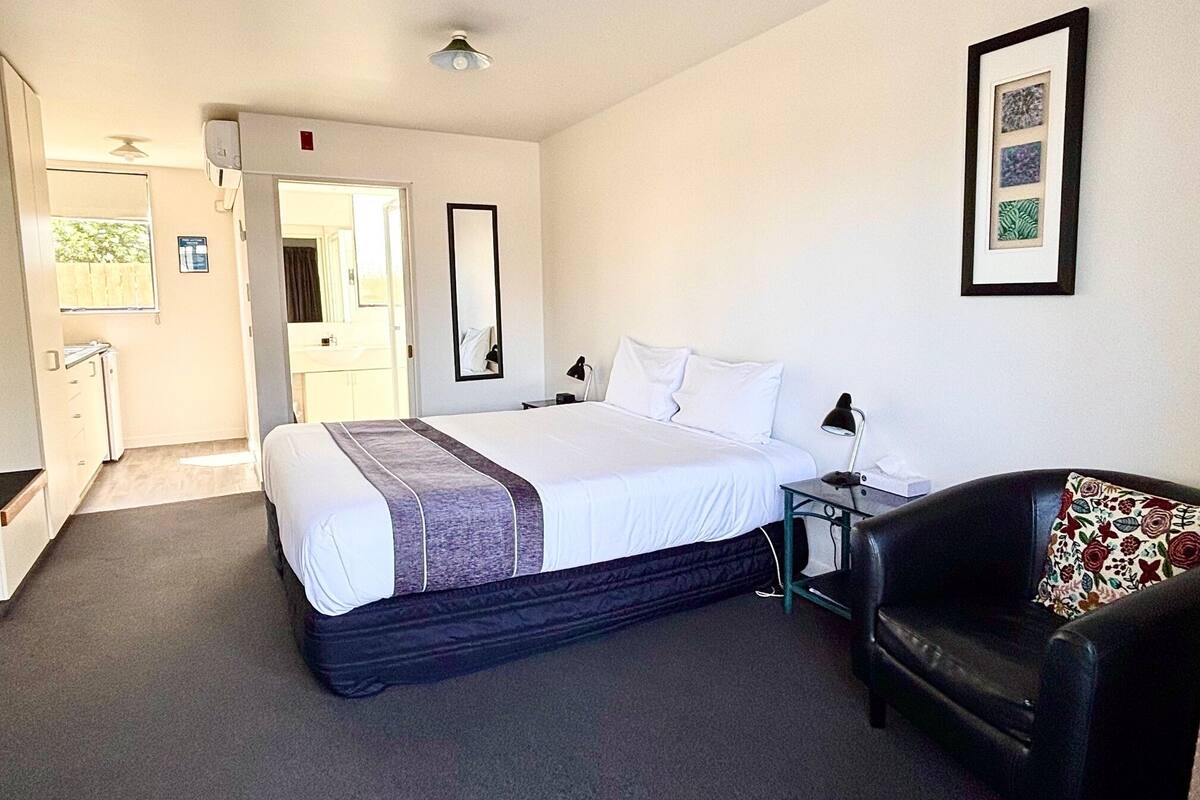 A hotel room with a bed, a desk, a chair, a mirror, and a framed picture on the wall.