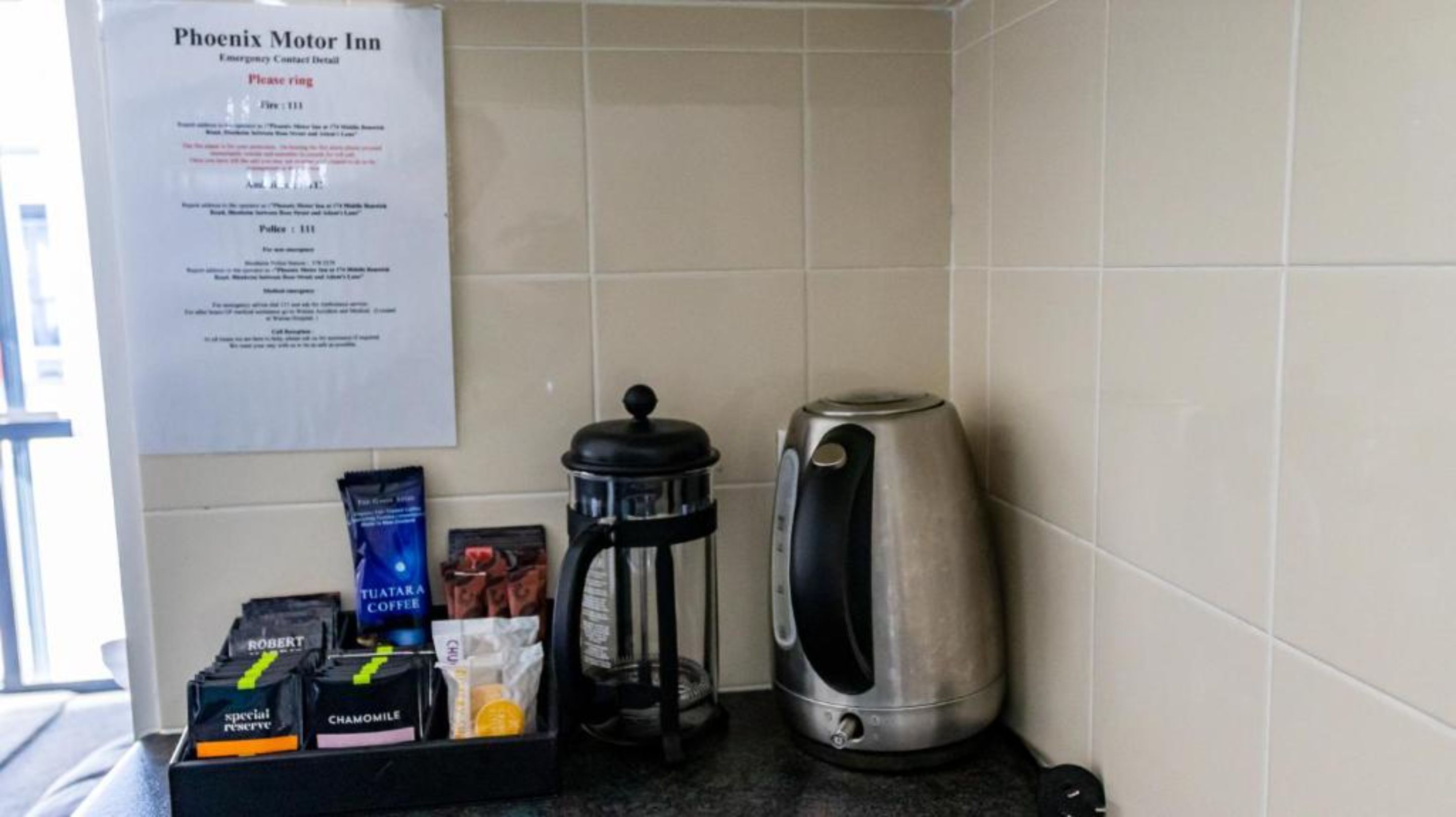 A coffee station with a sign, a coffee maker, and a kettle in a hotel room.