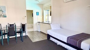 A room with a bed, a desk, and chairs. There is a window and an air conditioning unit on the wall.