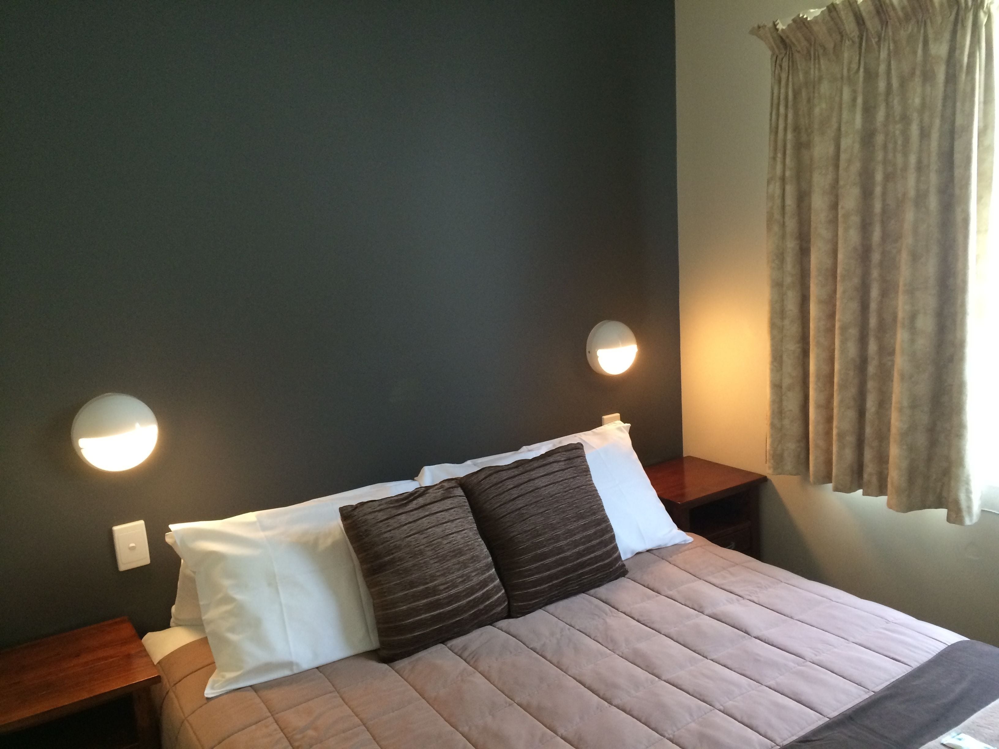 A neatly made bed with a striped pillow and a white pillow, flanked by two bedside tables with wall-mounted lamps.