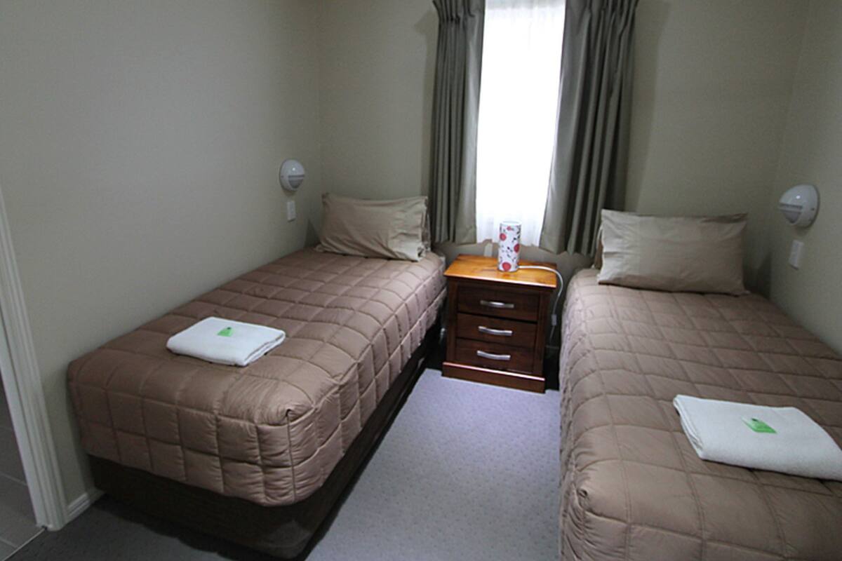 Una habitación de hotel con dos camas, una mesita de noche de madera y una ventana con cortinas.