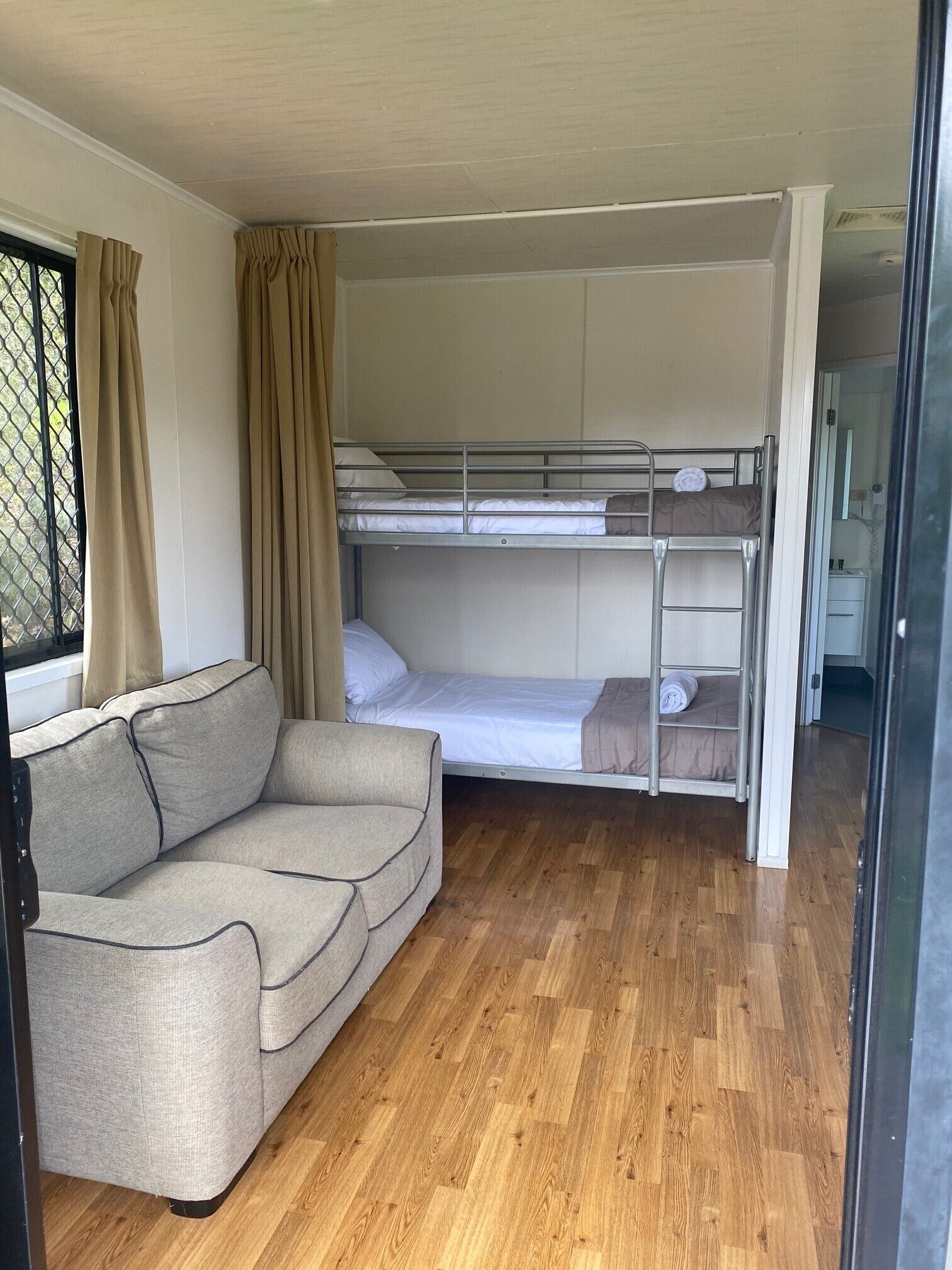 Une petite pièce avec un lit superposé, un canapé et une fenêtre avec des rideaux.