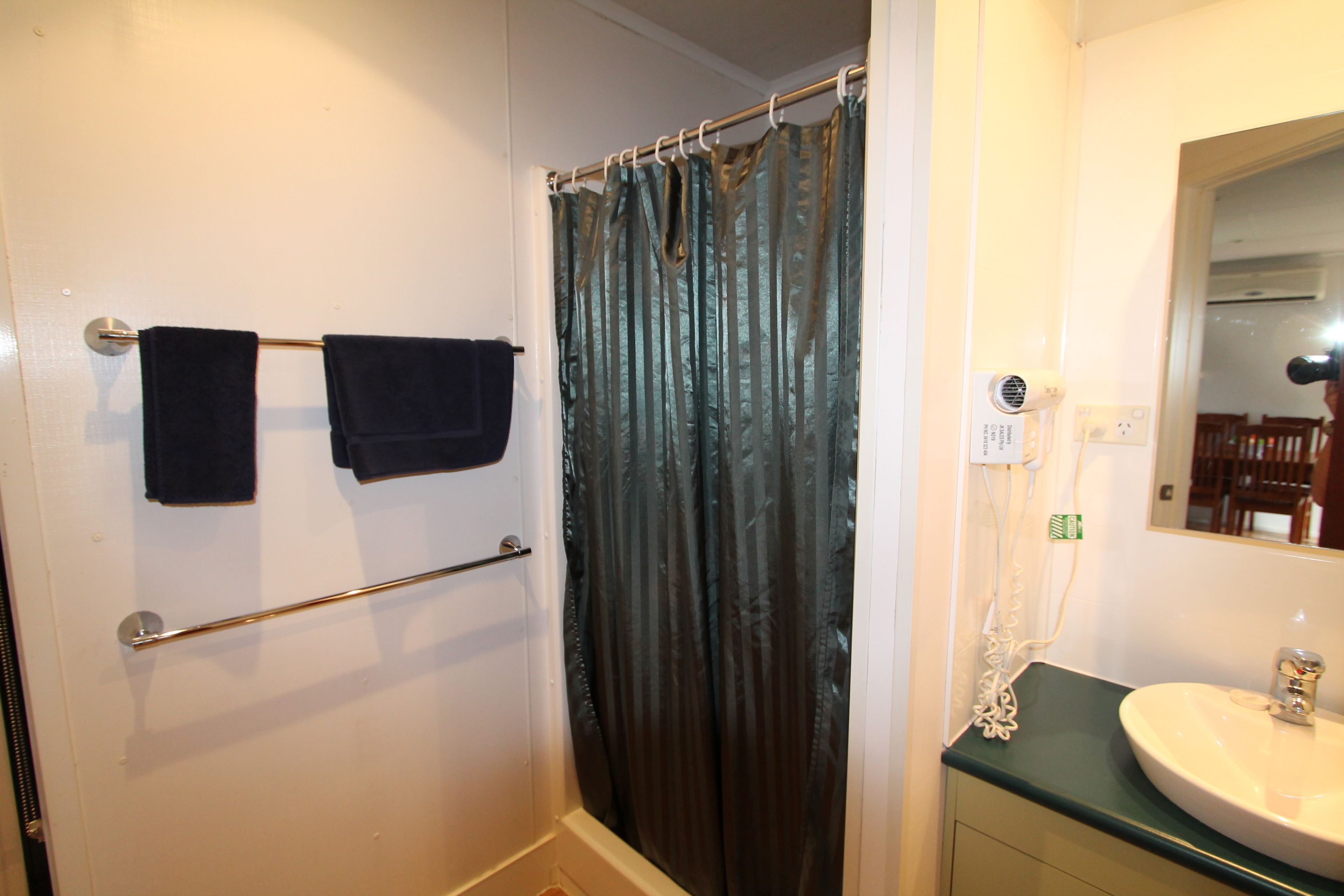 Un baño con cortina de ducha, un toallero con dos toallas, un lavabo y un espejo.