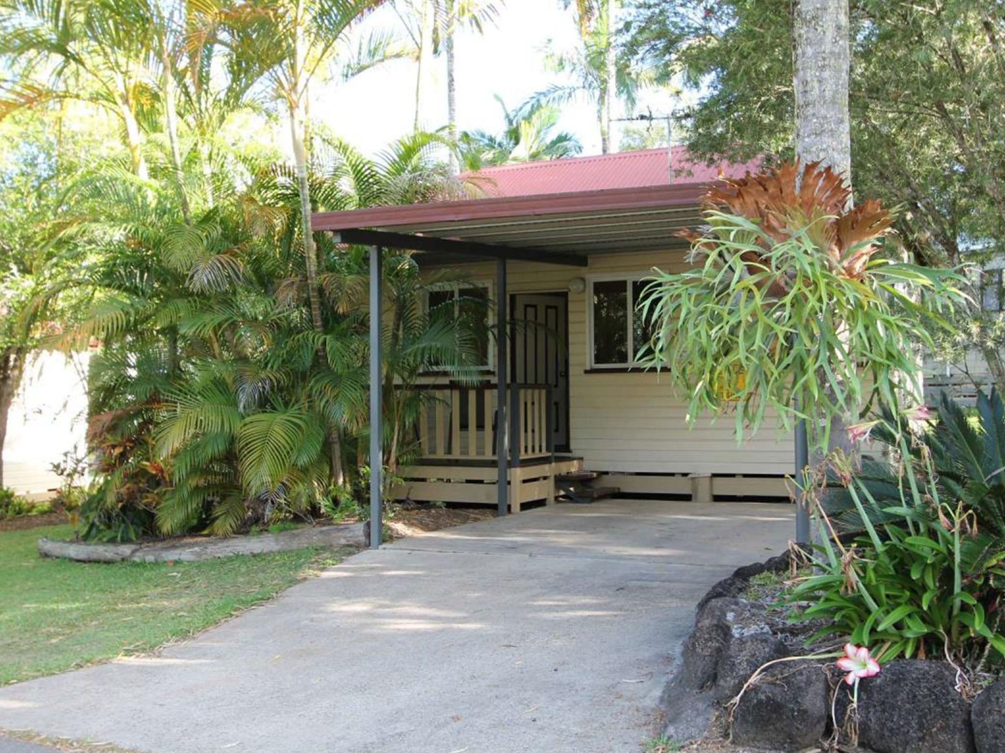 Une petite maison à un seul étage, dotée d’un porche et entourée d’une végétation tropicale luxuriante.