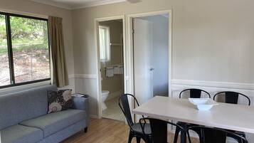 Une pièce avec un canapé gris, une table à manger avec quatre chaises, un ventilateur de plafond et une vue sur un jardin par la fenêtre.