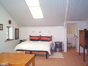 A bedroom with a bed, a wooden table, a window, and a door leading to another room.